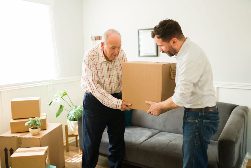 Older adult moving into Garden Valley with family assistance, carrying boxes together in a bright living room — senior living Boise.