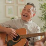 An older Asian man joyfully plays an acoustic guitar and sings in a cozy indoor gathering, showcasing the vibrant community life of Independent Living in Boise.