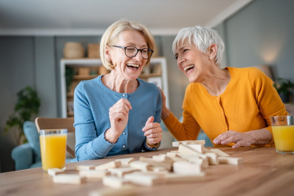 Two older adults laughing together while playing a game, representing the joy and connection found through independent living perks.