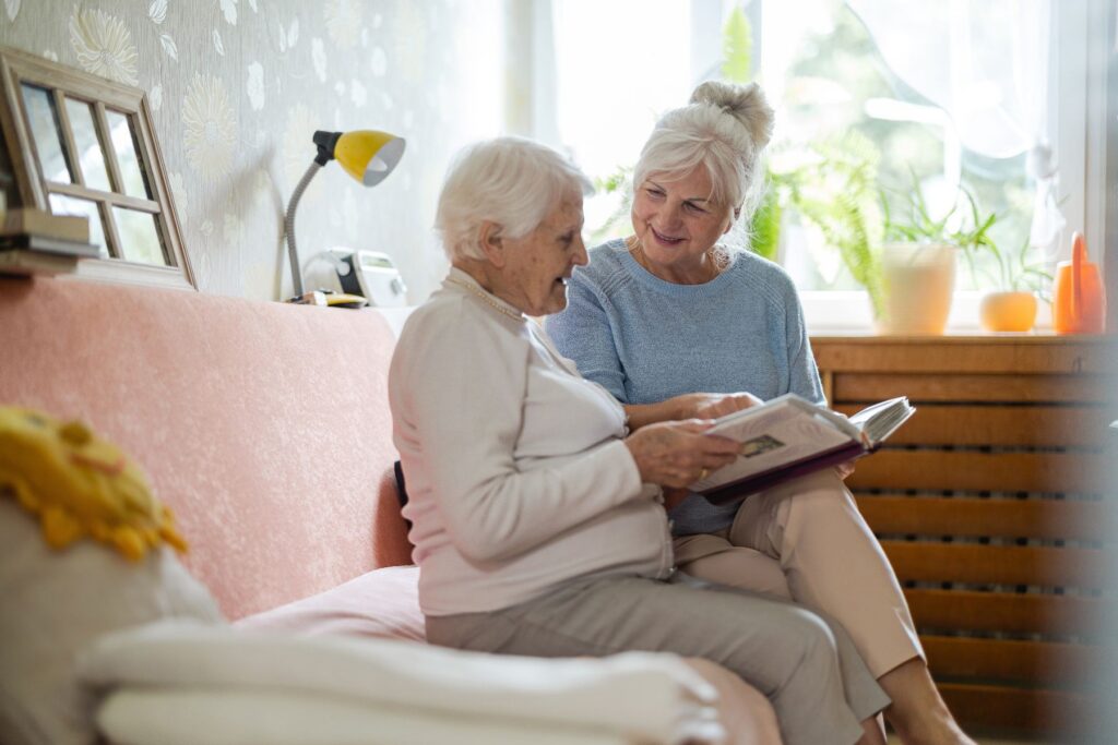 Caregiver and older woman reviewing a photo album together while reevaluating senior living needs.