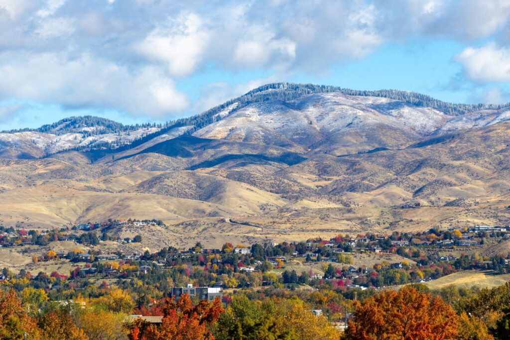 A picturesque autumn landscape in Boise, ID, featuring vibrant fall foliage, suburban hillside communities, and snow-dusted mountain peaks, reflecting the scenic environment and lifestyle opportunities in senior living communities.